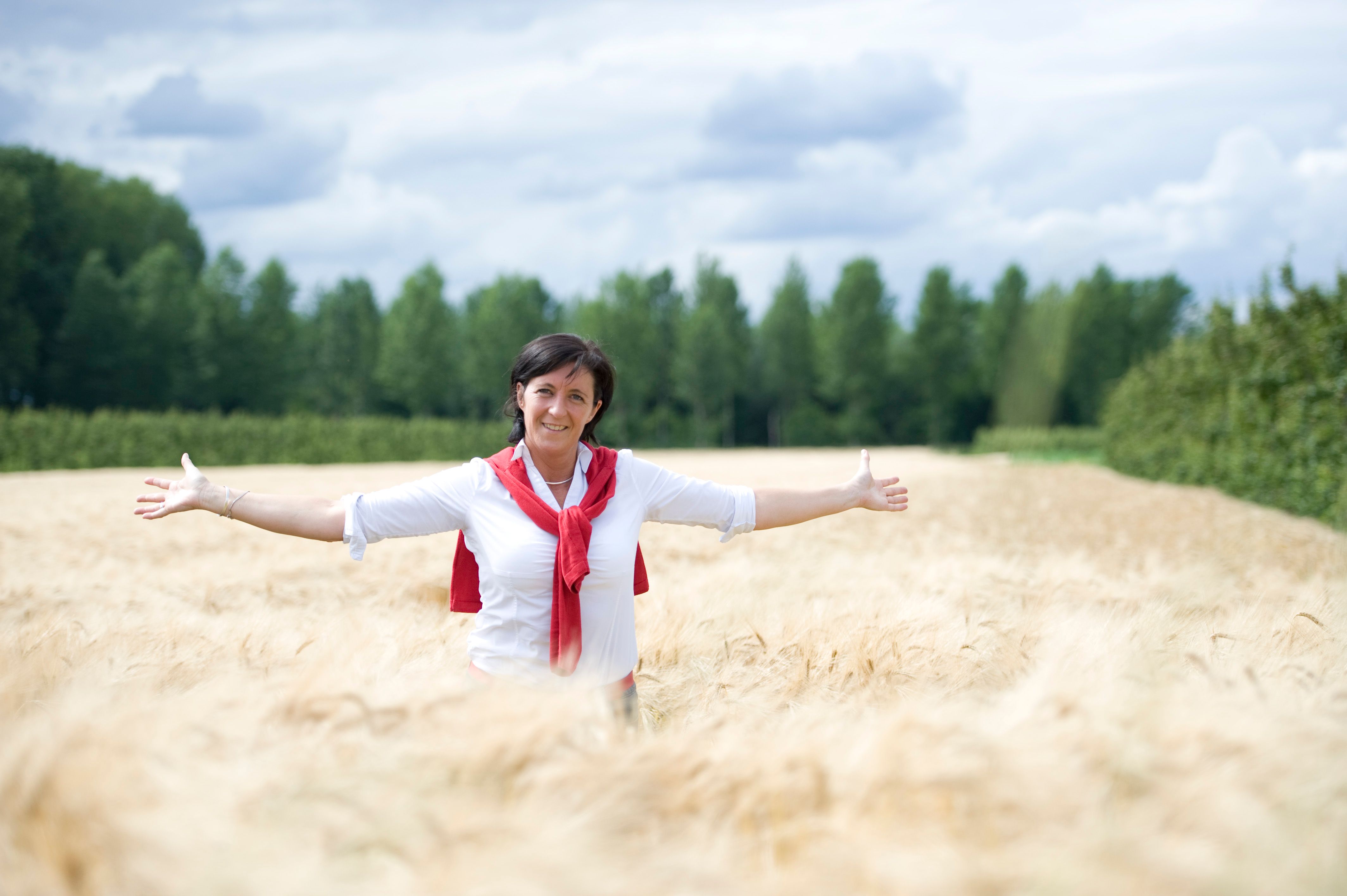 Cheerful woman with arms spread open in a field, feeling free to say yes to life's adventures